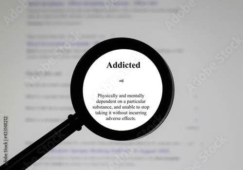 Selective focus on word addicted, word in a dictionary. Close up of an English dictionary page with the word addicted