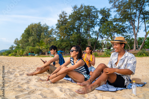 Group of Happy Asian man and woman friends sitting on the beach enjoy picnic and talking together at summer sunset. Male and female friendship relax and having fun summer outdoor lifestyle activity.