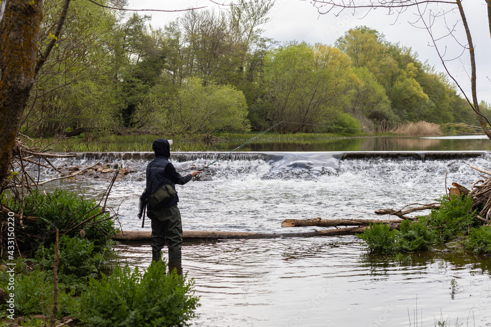 young teenager casting fishing rod into stream with small waterfall at sunset with copy space young teenager casting fishing rod into stream with small waterfall at sunset with copy space