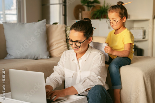 Work life balance. Young happy woman loving mother working remotely from home with little daughter, smiling mom freelancer and kid looking at laptop while sitting together in living room