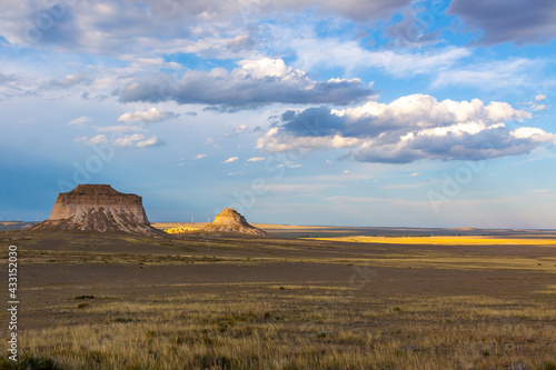 Pawnee Buttes in Pawnee National Grassland, on the great plains of Colorado with clouds forming against a blue sky and the sunlight highlighting one area of the landscape