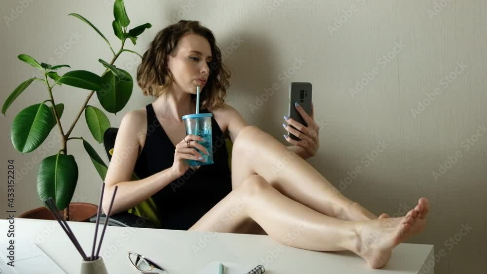 Attractive young woman smiles, poses, takes selfies and streams video to social media from her smartphone. Closeup portrait of happy woman with coktail in swimwear making photo in home office Attractive young woman smiles, poses, takes selfies and streams video to social media from her smartphone. Closeup portrait of happy woman with coktail in swimwear making photo in home office