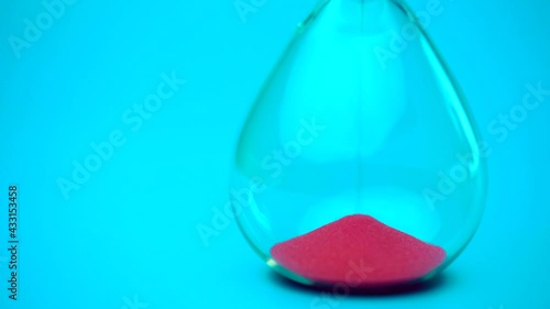 Sand flowing through the hourglass, measuring the elapsed time in the countdown to the deadline on a blue background.
