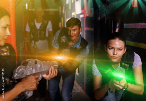 positive young friends standing with laser guns during laser tag game in dark room