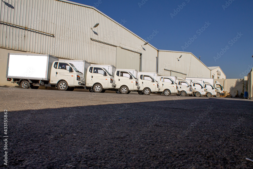 closeup of trucks lined up. park trucks. facade of an factory building and warehouse with freight cars in length closeup of trucks lined up. park trucks. facade of an factory building and warehouse with freight cars in length