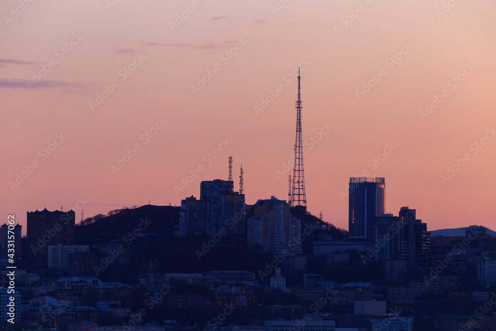 Dawn in Vladivostok. The Vladivostok TV tower stands on a hill among residential buildings in the city center. City built-up hill at dawn.
