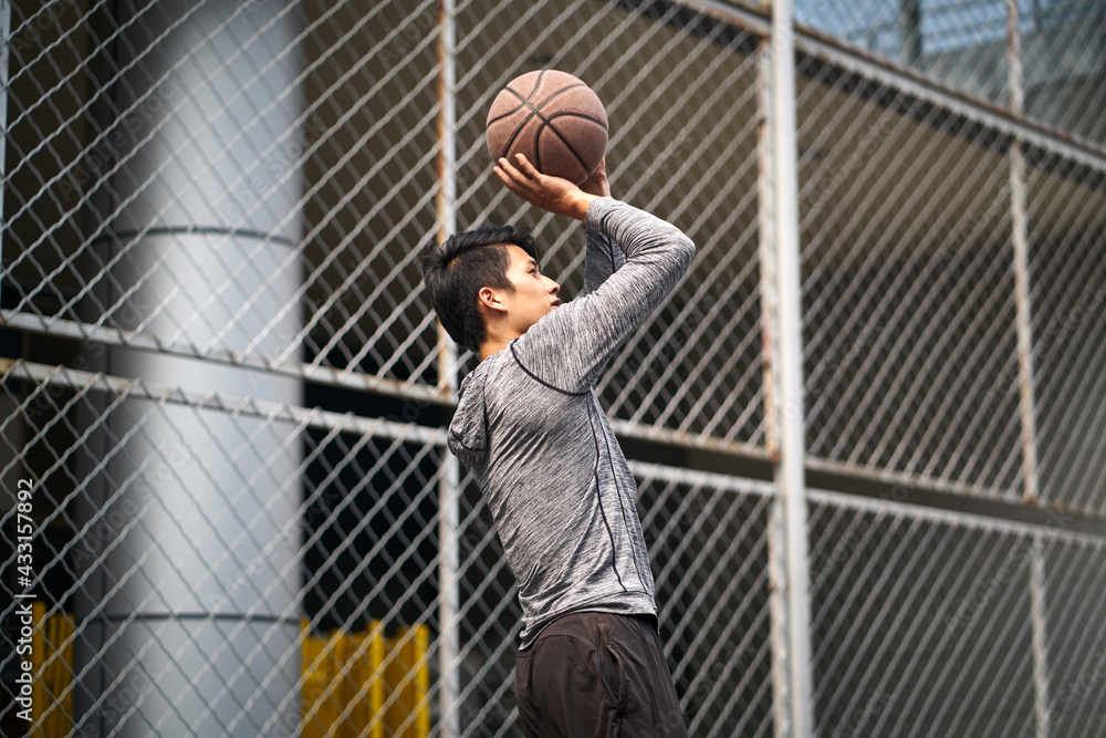 asian young basketball player taking a jump shot on outdoor court asian young basketball player taking a jump shot on outdoor court