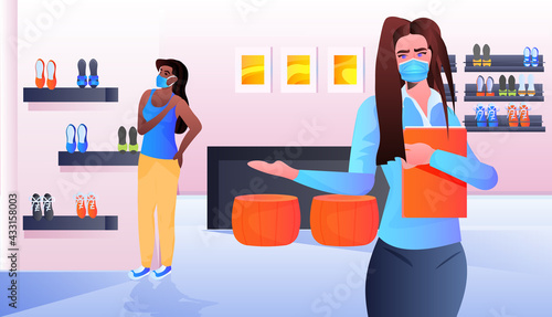 saleswoman in mask showing clothes to african american customer in fashion boutique coronavirus pandemic
