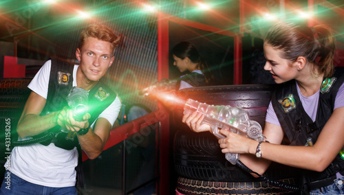 Group portrait of glad emotional people with laser guns playing laser tag game together in dark labyrinth