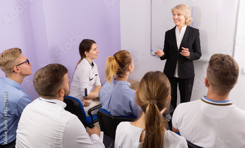 Glad pleasant female speaker giving presentation for cheerful positive students in lecture hall