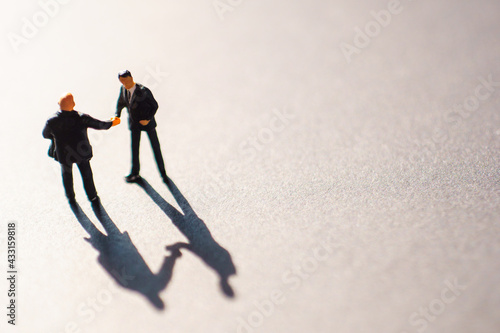 Silhouettes of two businessman, probably men, shaking their hands as a sign of an agreement or deal. The meeting takes place on floor  during the warn sunset.