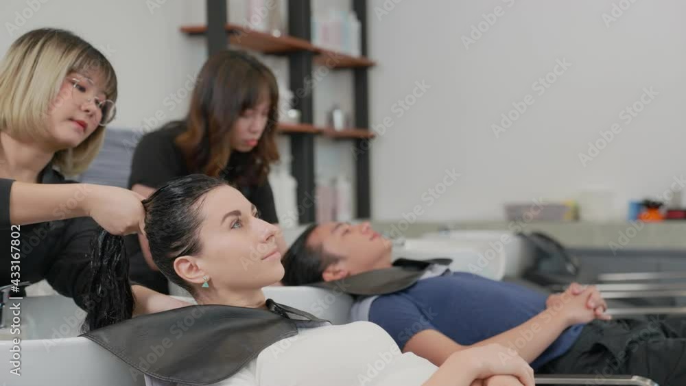 The female beautician washing the caucasian client hair with hair conditioner, while waiting to ferment, Barber gives a relaxing massage to the nape of neck so client heals the stiffness and fatigue. The female beautician washing the caucasian client hair with hair conditioner, while waiting to ferment, Barber gives a relaxing massage to the nape of neck so client heals the stiffness and fatigue.