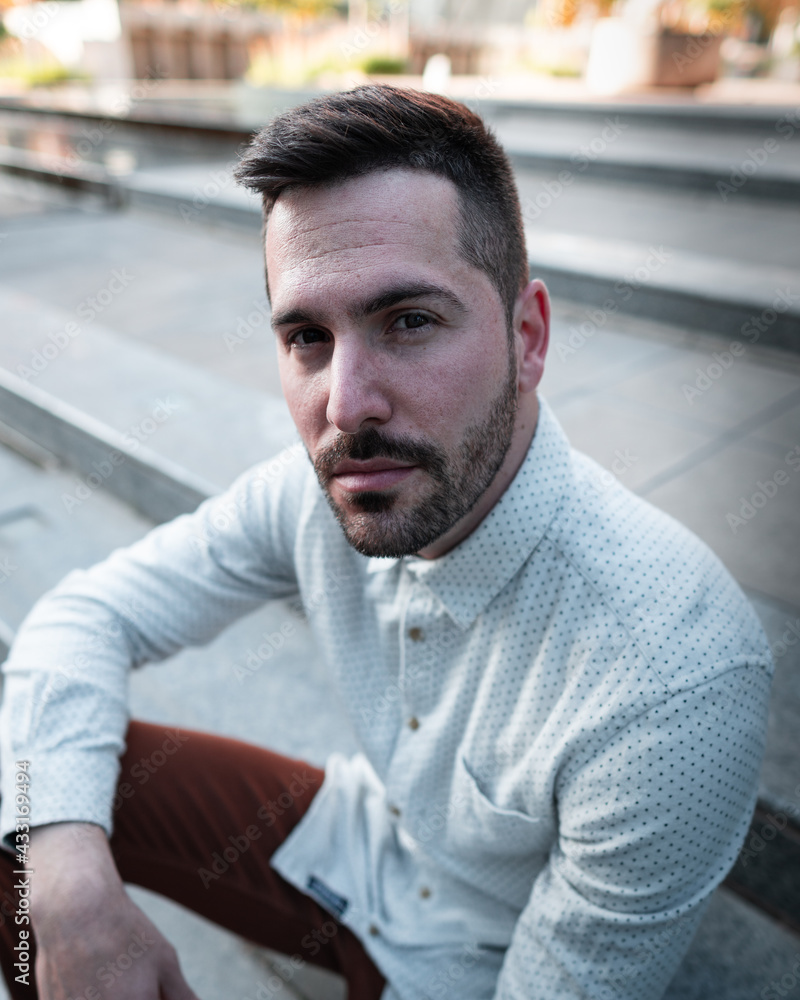 Portrait of a seated man in the stairs in the financial district at sunset time with a white t-shirt and brown pants Portrait of a seated man in the stairs in the financial district at sunset time with a white t-shirt and brown pants