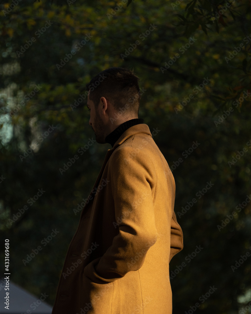 Fototapeta premium Fall portrait of a bearded man with a brown coat at sunset time in the park