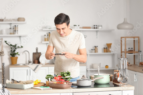 Young man taking photo of fresh vegetables in kitchen