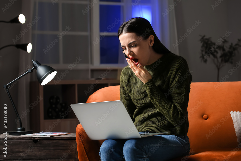 Sleepy young woman with laptop at home late in evening. Concept of addiction