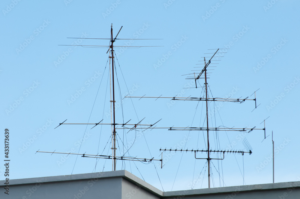 Two TV antennas at rooftop on a blue sky background Two TV antennas at rooftop on a blue sky background