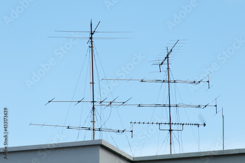 Two TV antennas at rooftop on a blue sky background