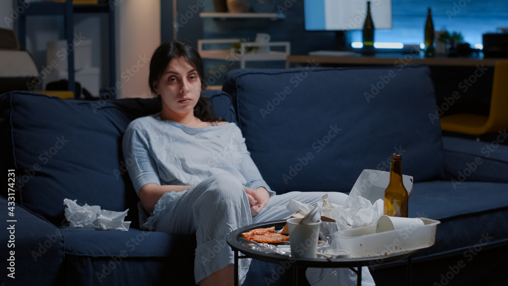 Fototapeta premium Traumatised, frustrated depressed woman looking at camera sitting alone on sofa thinking at loneliness feeling emotionally unstable, lonely desperate vulnerable suffering from anxiety, chronic disease