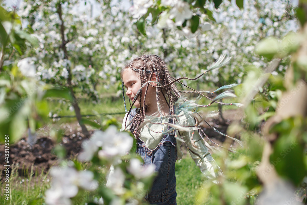 Pretty preteen girl walking in the blooming apple garden in spring, relax and freedom, beauty of nature. Happy kid enjoying flower blossom in fruit orchard at sunny day. Spring outdoor