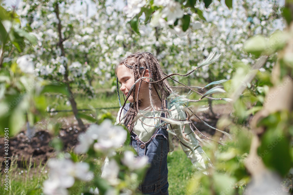 Pretty preteen girl walking in the blooming apple garden in spring, relax and freedom, beauty of nature. Happy kid enjoying flower blossom in fruit orchard at sunny day. Spring outdoor Pretty preteen girl walking in the blooming apple garden in spring, relax and freedom, beauty of nature. Happy kid enjoying flower blossom in fruit orchard at sunny day. Spring outdoor