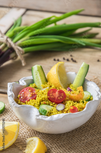 Couscous salad with cucumber  tomatoes and onions in a white bowl on rustic wooden background  vertical