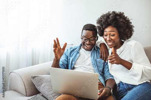 Young couple sitting in their living room with laptop waving to their marital therapist after successful online therapy and saved marriage. Shot of a smiling young couple using a laptop while relaxing