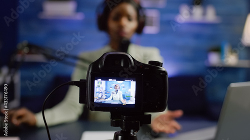 African influencer recording blog looking at professional camera at online talk show home studio. Social media content creator streaming online broadcast, blogger discussing wearing headphones.
