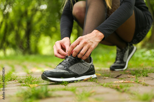 woman's hands tying the laces on the sneaker. woman's legs wearing sport sneakers outdoors