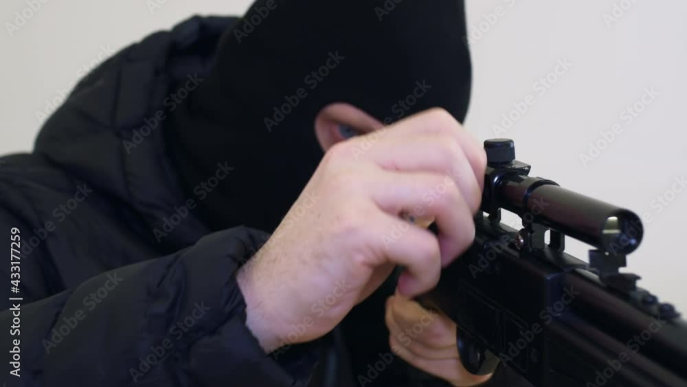 A killer in a black balaclava adjusts a sniper rifle, makes adjustments, twitches the bolt of the rifle and takes aim at the victim. Close-up of weapons. A killer in a black balaclava adjusts a sniper rifle, makes adjustments, twitches the bolt of the rifle and takes aim at the victim. Close-up of weapons.