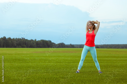 sport woman is doing yoga exercises on large grass field on sunset.