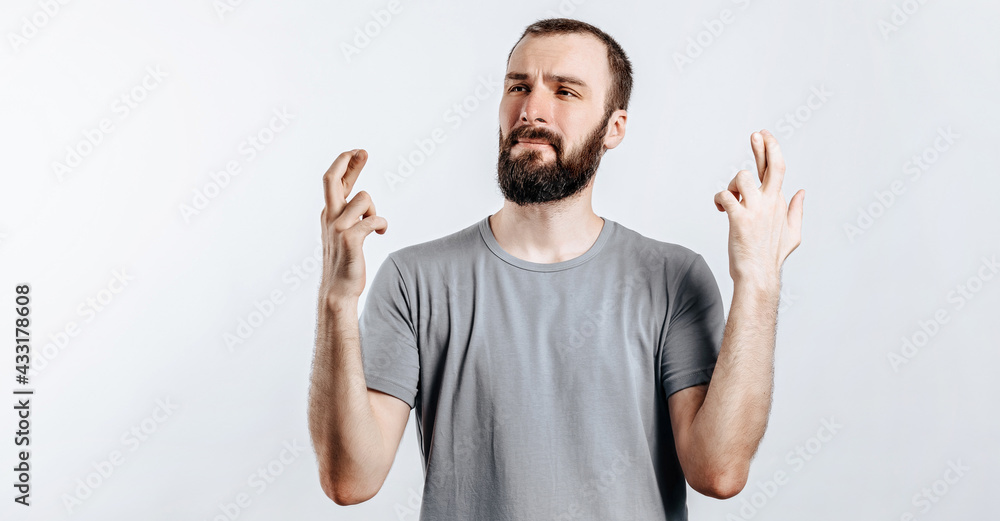 Naklejka premium Handsome young man frown and cross fingers in hope on white background with space for advertising mock up