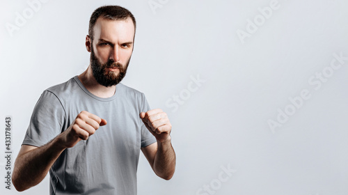 Portrait of handsome young man frowning while looking at camera holding fists and boxing on white background with space for advertisement mock up