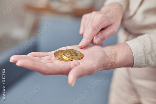 Old woman holds bitcoin coins in her hand. Senior citizen happy life concept
