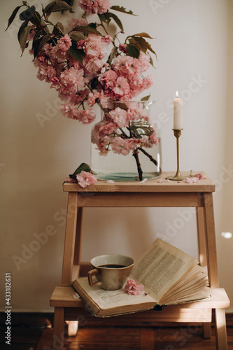 Fototapeta Naklejka Na Ścianę i Meble -  a small wooden staircase with a transparent vase and blooming pink branches. composition of sakura branches in a transparent vase and an open book with a cup of coffee. pink sakura petals. copy space