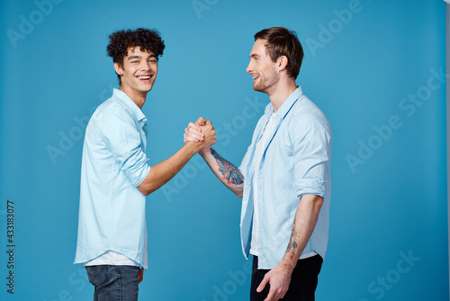 Happy friends in identical shirts shake hands on a blue background communication