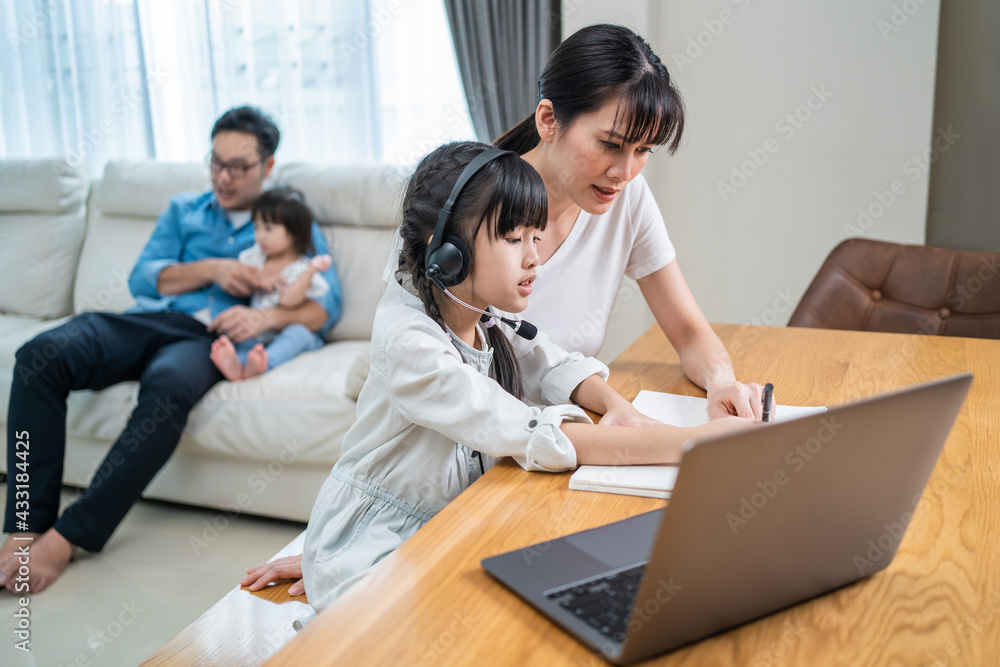 Asian mother teaching daughter doing homework while learning online.