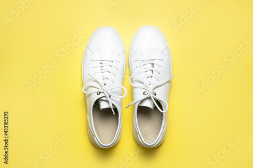 White sneakers on yellow background top view flat lay. Stylish youth women's leather sneakers, sports shoes, genuine leather footwear. Minimalistic shoe store advertising fashion style Shoe background