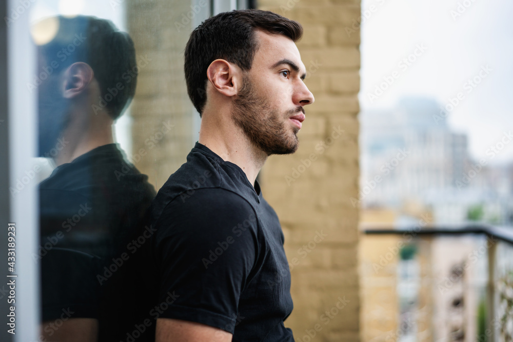 Porter of handsome serious young brunette man with a beard in a black t-shirt on the balcony with city view Porter of handsome serious young brunette man with a beard in a black t-shirt on the balcony with city view