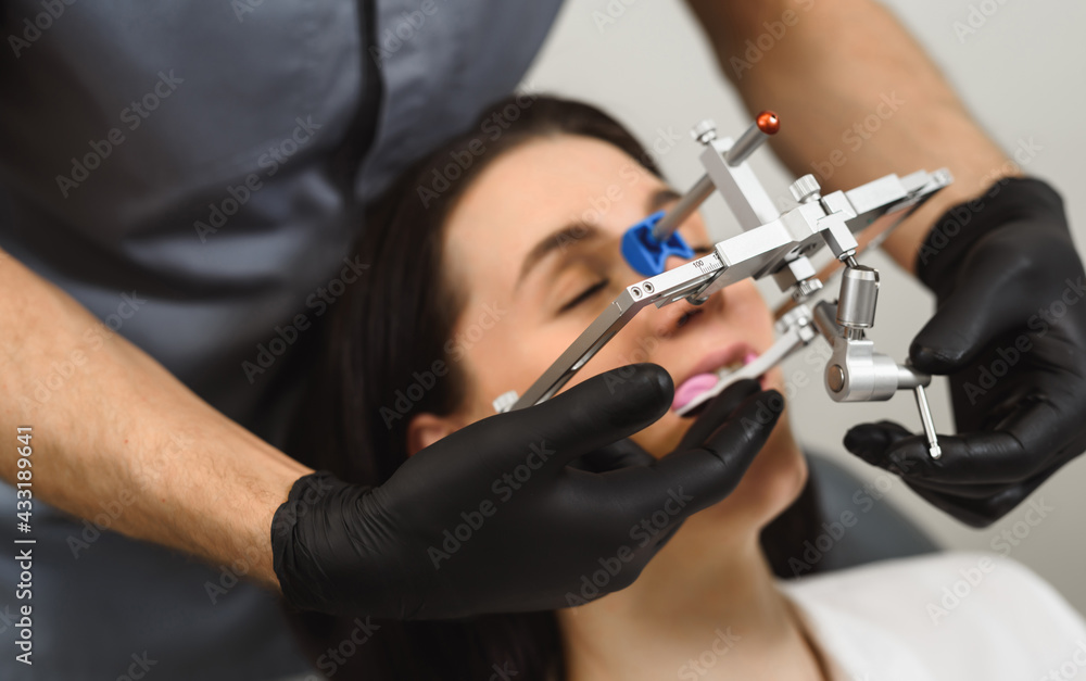 An experienced dentist placing a facial bow for woman patient to examine the bite. Modern technologies in dental treatment