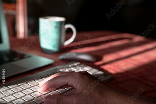 Computer laptop with woman hand on wireless keyboard, on orange table top. Work from home concept.