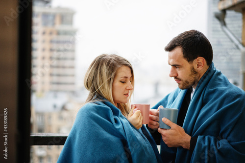 Young beautiful couple family man and woman sitting on the windowsill drinking coffee wrapped in blue blankets, romantic romantic at the hotel