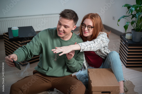 A cute girl and a guy show the keys to their new apartment in their smartphone and are happy with the purchase