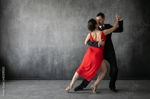 Couple of professional tango dancers in elegant suit and dress pose in a dancing movement on dark background. Attractive man and woman dance looking eye to eye.