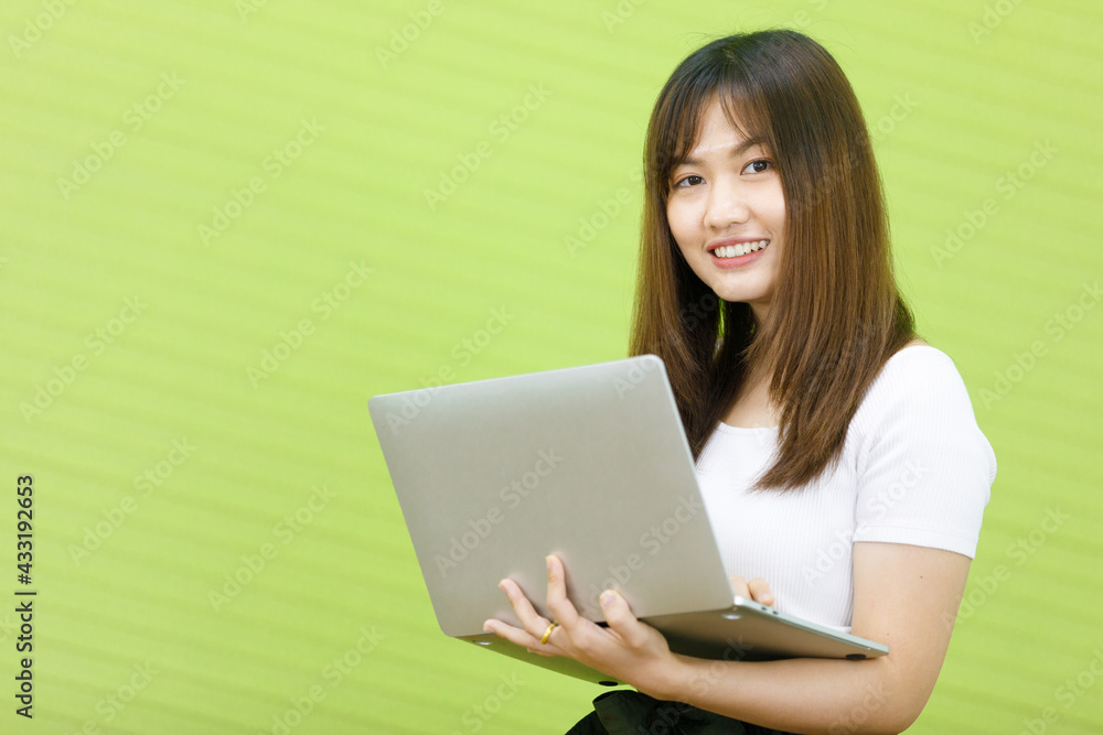 Asian smiling woman wearing holding and looking at laptop computer. Lady asia standing is happy to working in green background. Asian smiling woman wearing holding and looking at laptop computer. Lady asia standing is happy to working in green background.