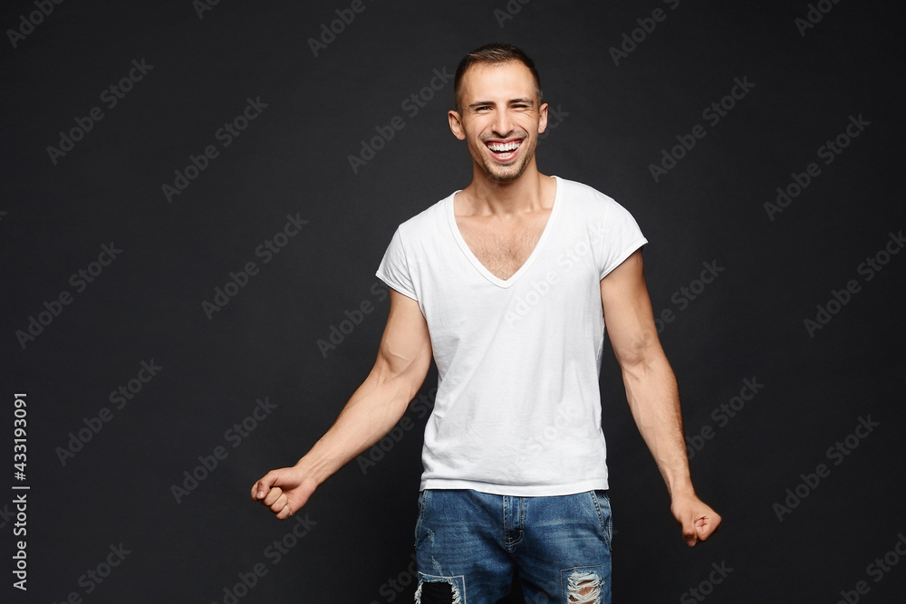 Happy guy in white t-shirt isolated at dark background. A handsome young man with a broad smile and snow-white teeth posing in the black background in a casual outfit. Happy guy in white t-shirt isolated at dark background. A handsome young man with a broad smile and snow-white teeth posing in the black background in a casual outfit.
