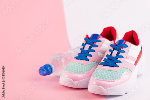 Sport accessories sport shoes, bottle of water on pink and white background. Sport, healthy lifestyle, fitness, exercise, workout concept. Female sport equipment