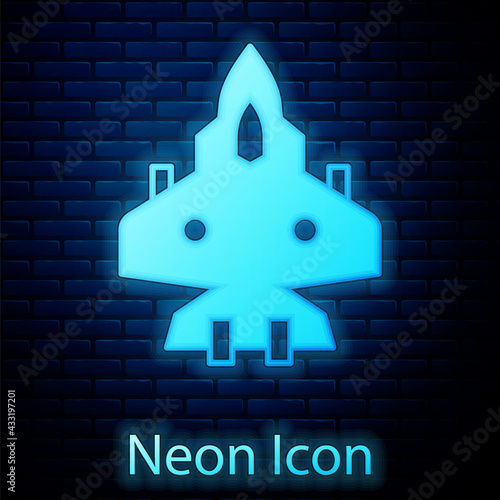 Glowing neon Jet fighter icon isolated on brick wall background. Military aircraft. Vector