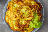 Fritters from zucchini in grey plate with sour cream sauce and greens. Vegetable pancakes of courgettes with green salad