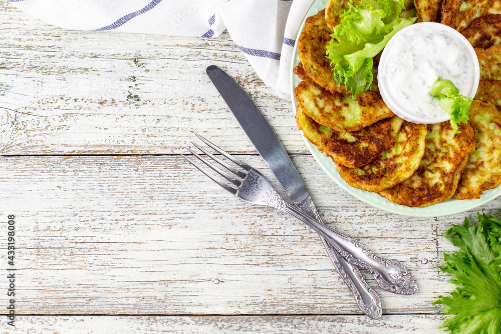 Fritters from zucchini with sour cream sauce and greens. Vegetable pancakes of courgettes with green salad